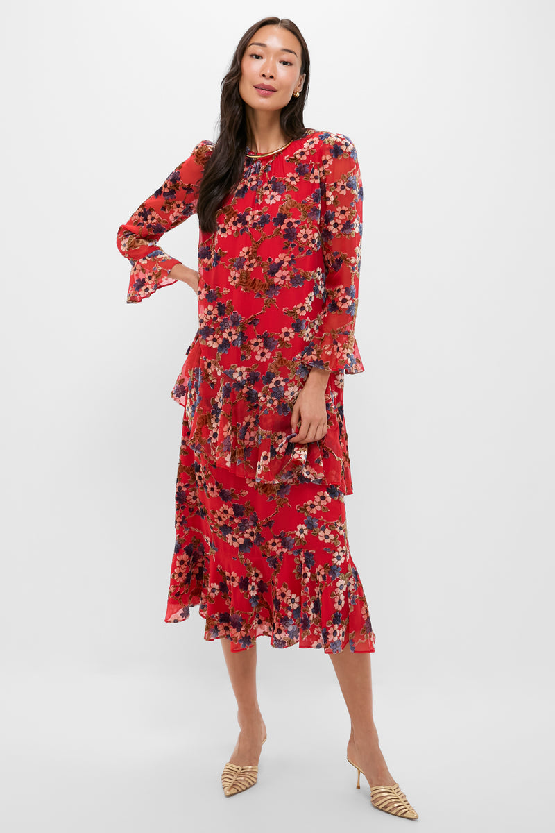 A woman in a Tuckernuck ruffled midi dress with red florals and layered details, paired with beige pointed-toe heels, stands against a plain background.
