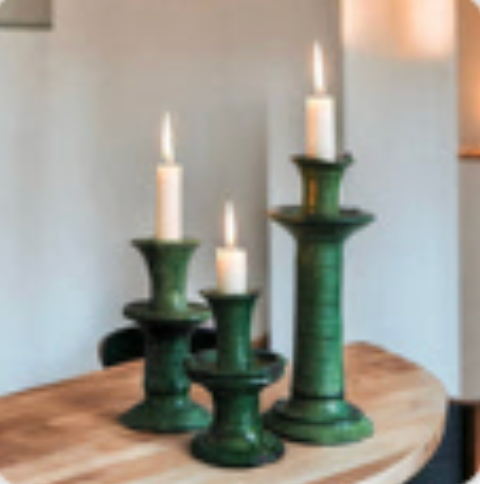 Three green ceramic candle holders by Tuckernuck Vintage Accessories, each with a lit white candle and varying in height, are displayed on a wooden surface against a neutral backdrop.
