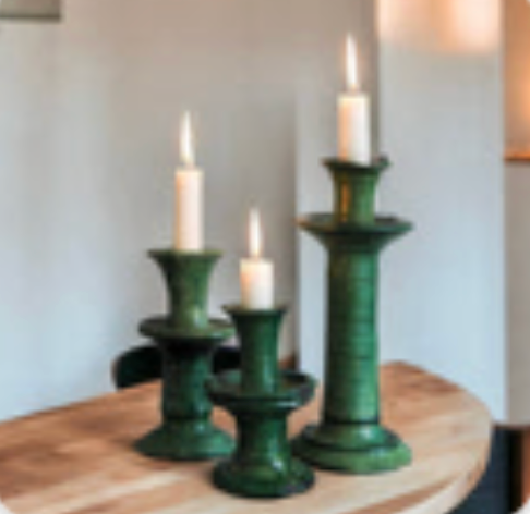 Three green ceramic candle holders from Tuckernuck Vintage Accessories, each at a different height with a white candle, are arranged on a wooden table against a neutral background.
