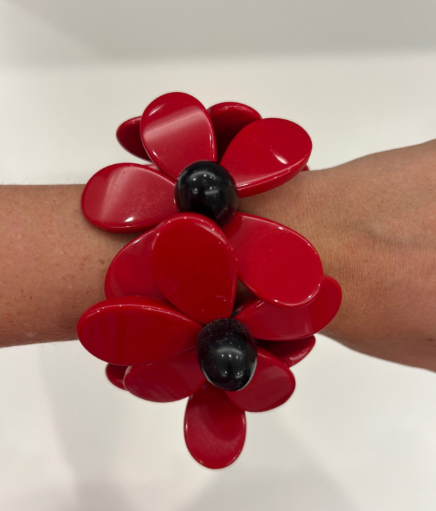 A wrist adorned with a Tuckernuck Vintage Accessories bracelet, featuring large red flower-shaped petals and black bead centers.