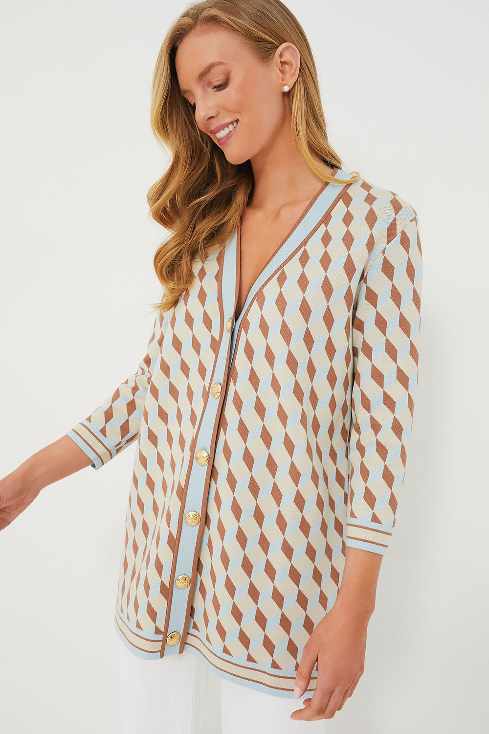 A woman wears the Tuckernuck Ocean Spray Knit Geo Liv Cardigan, featuring a geometric print in light blue, brown, and beige with gold buttons and three-quarter sleeves.