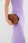 Person holds the Cocoa Origami Scallop Clutch, a classic, high-end, shell-shaped woven bag, paired with a form-fitting dress, embodying effortless elegance and fun style.