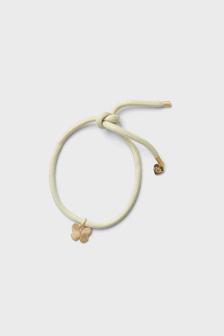 A pale yellow hair tie from HART features a gold butterfly charm and a small round gold tag on the elastic band, creating a playful bracelet-like accessory.