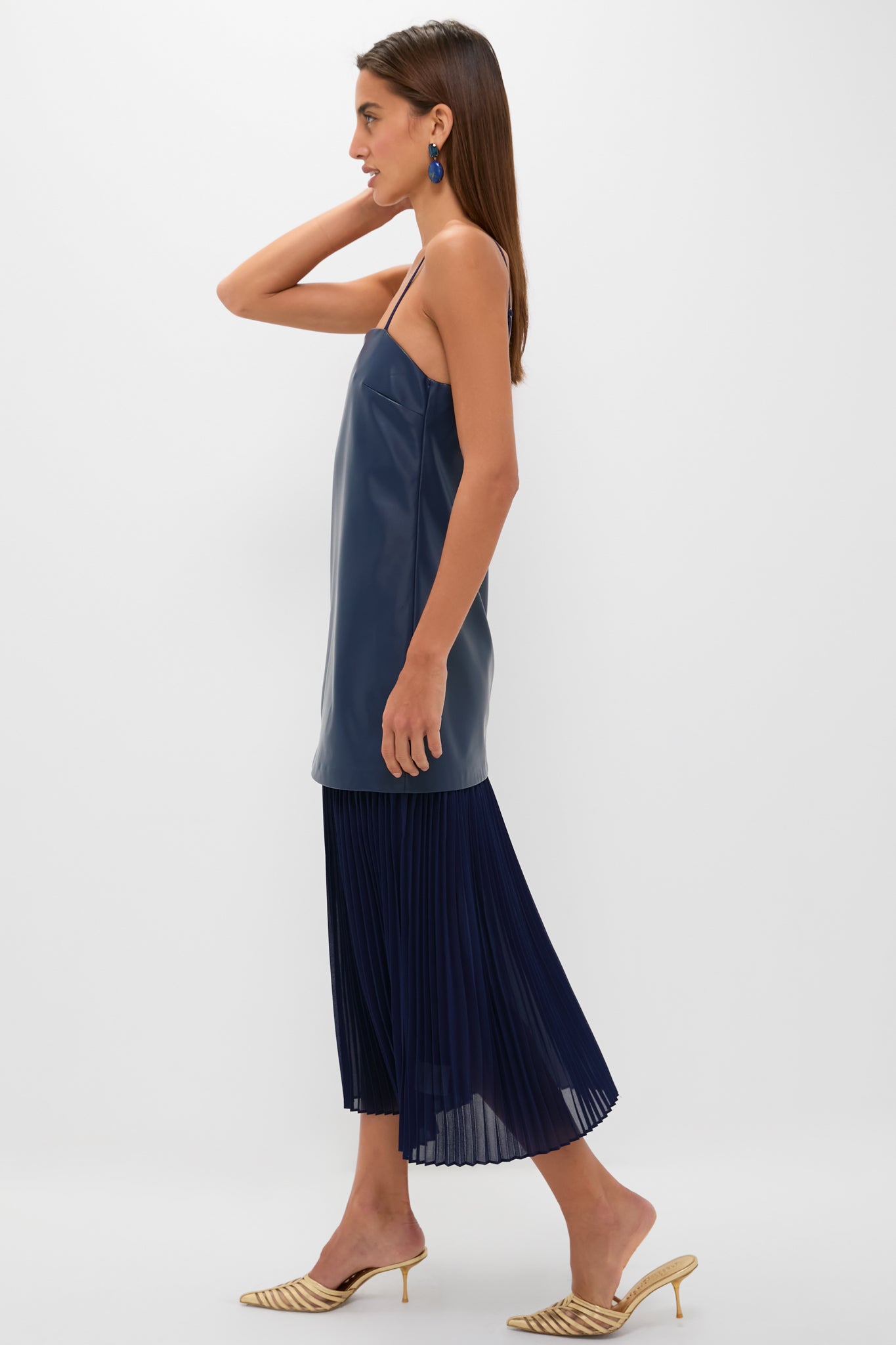 Model wears the Mixed Media Leather Pleated Ozzy Midi Dress, featuring a classic, effortless style with a fun leather-look top and pleated skirt, paired with high-end gold heels.
