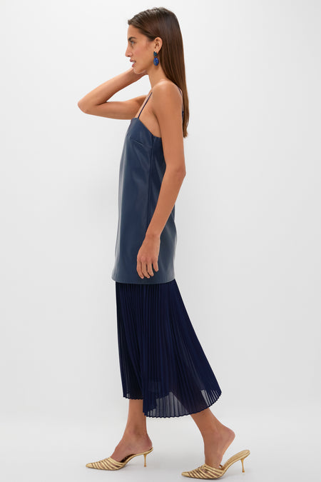 Model wears the Mixed Media Leather Pleated Ozzy Midi Dress, featuring a classic, effortless style with a fun leather-look top and pleated skirt, paired with high-end gold heels.