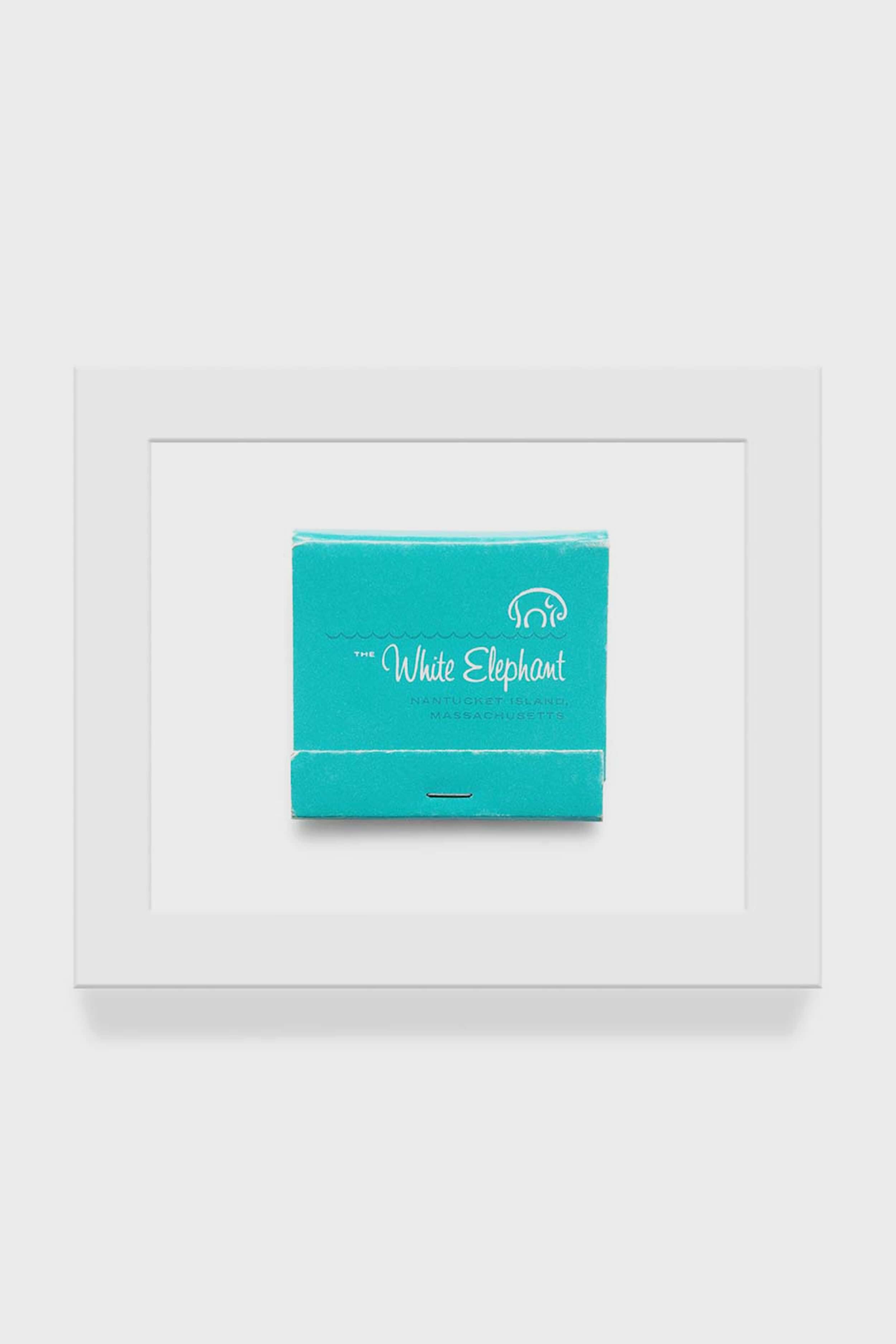 A framed macro photo from Matchbook Diaries by Charles Ryan Clarke features a turquoise White Elephant Nantucket matchbook print, elegantly centered with a white elephant logo.