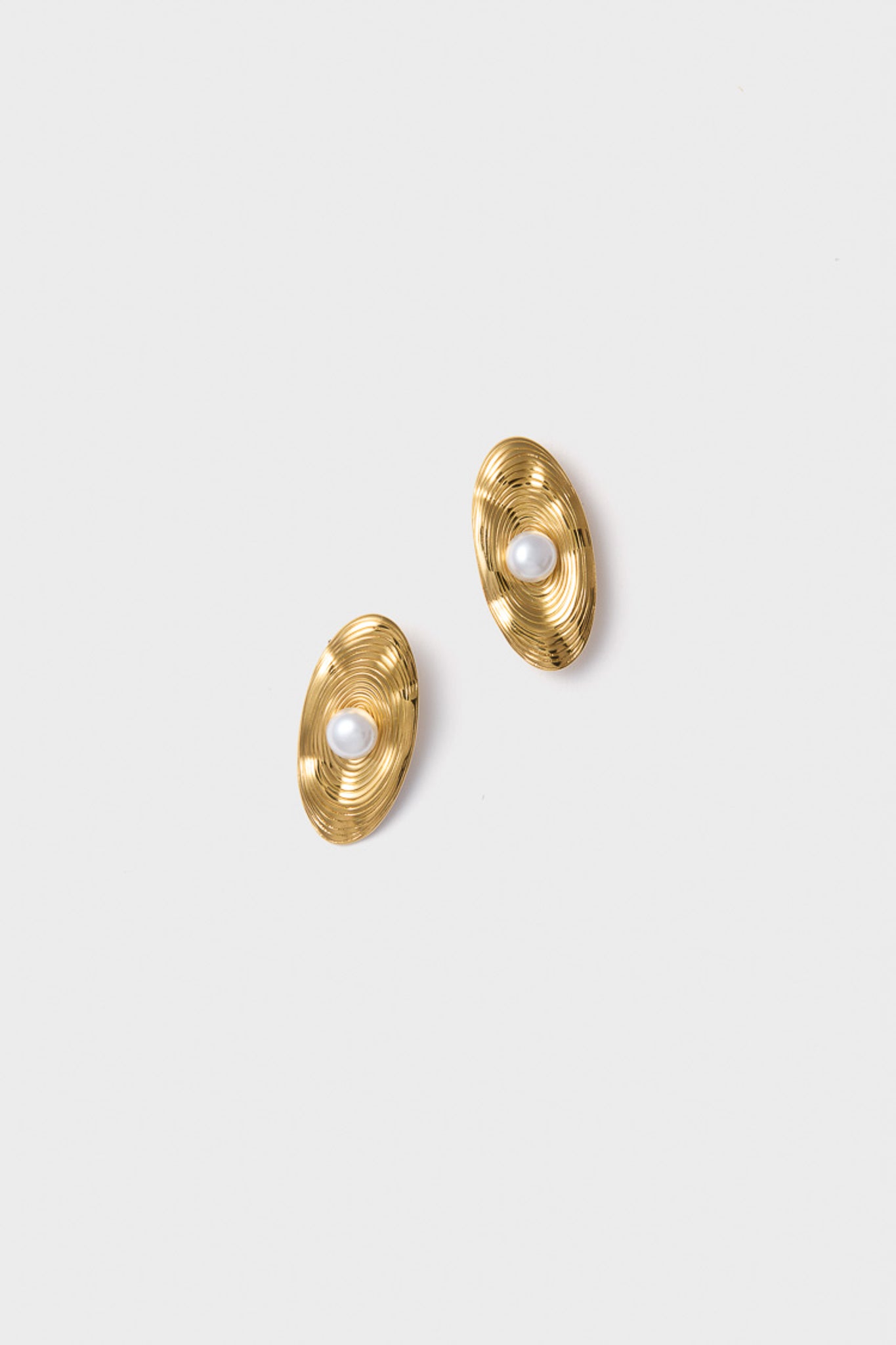 Petit Moments offers textured gold oval stud earrings with concentric ridges and a central white pearl, featuring a modern pearl earring design.
