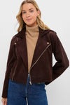 A woman faces the camera in a Hyacinth House dark brown faux suede boxy jacket, layered over a beige turtleneck and blue jeans—an essential autumn look.