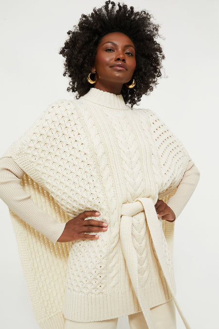 A woman wears an IrelandsEye Knitwear cream cable knit sweater featuring a belted waist and wide sleeves, expertly crafted from quality yarn inspired by classic Irish knitwear.