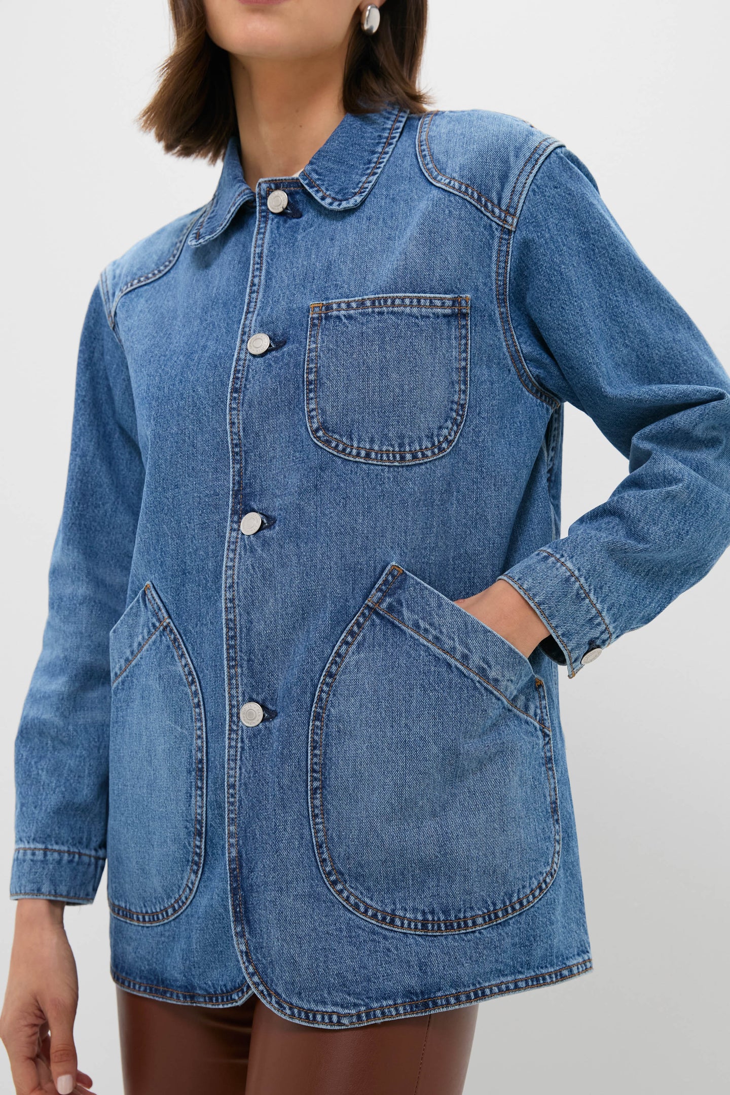 A person in a Twin Doves Denim blue vintage stonewash jacket with three front pockets and silver buttons, paired with relaxed fit brown pants.