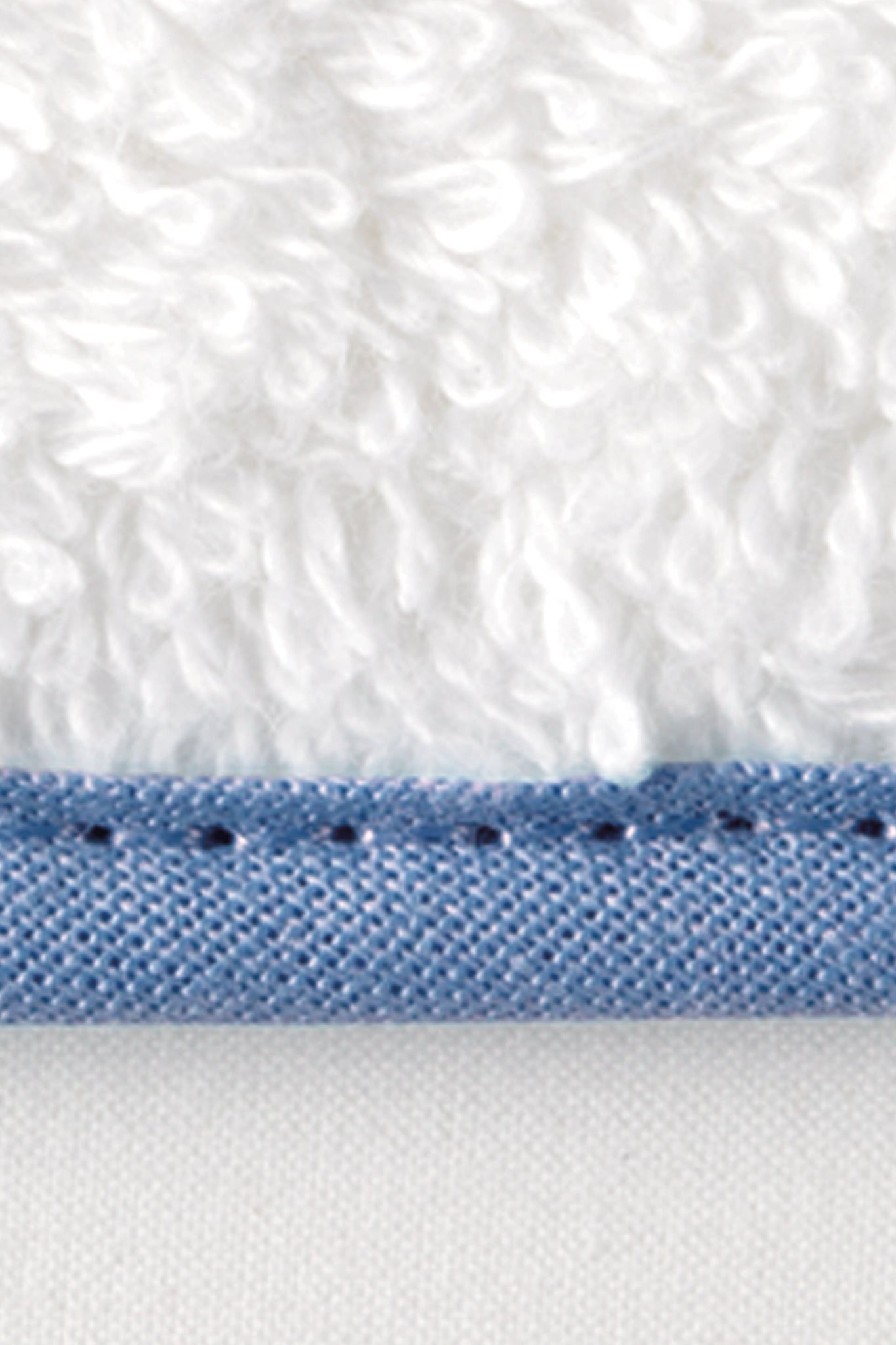 A close-up of a white bath towel made from terry cloth, featuring a textured surface and a blue stitched edge at the bottom.
