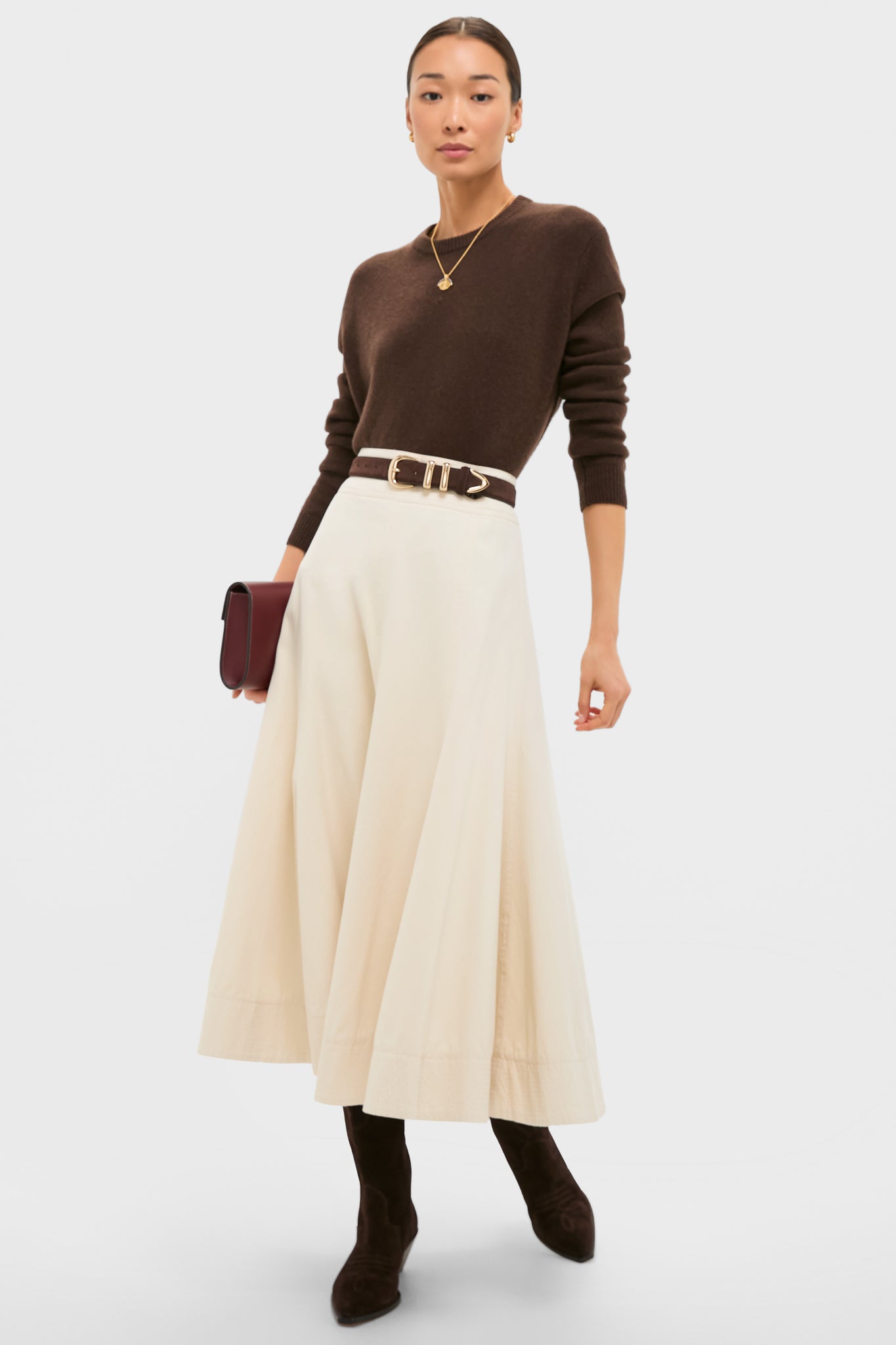 Model wearing classic Dark Espresso Suede Wilson Cowboy Boots with Western seam detailing, paired with an effortlessly chic outfit, including a cream midi skirt and a burgundy clutch.