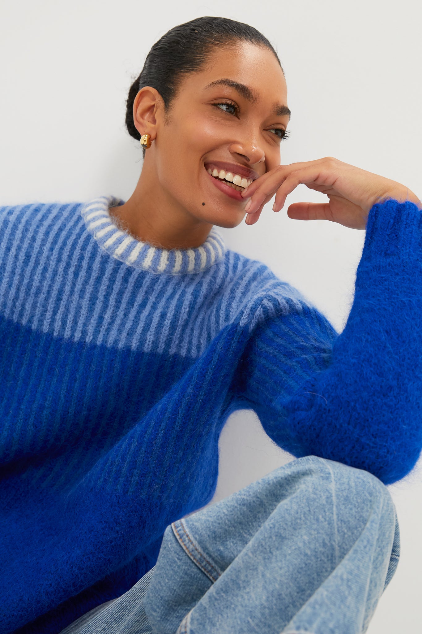 Smiling woman in cozy Blue Cocha Sweater, showcasing a classic and effortless style with ribbed pattern and mock neck, paired with light-wash jeans.