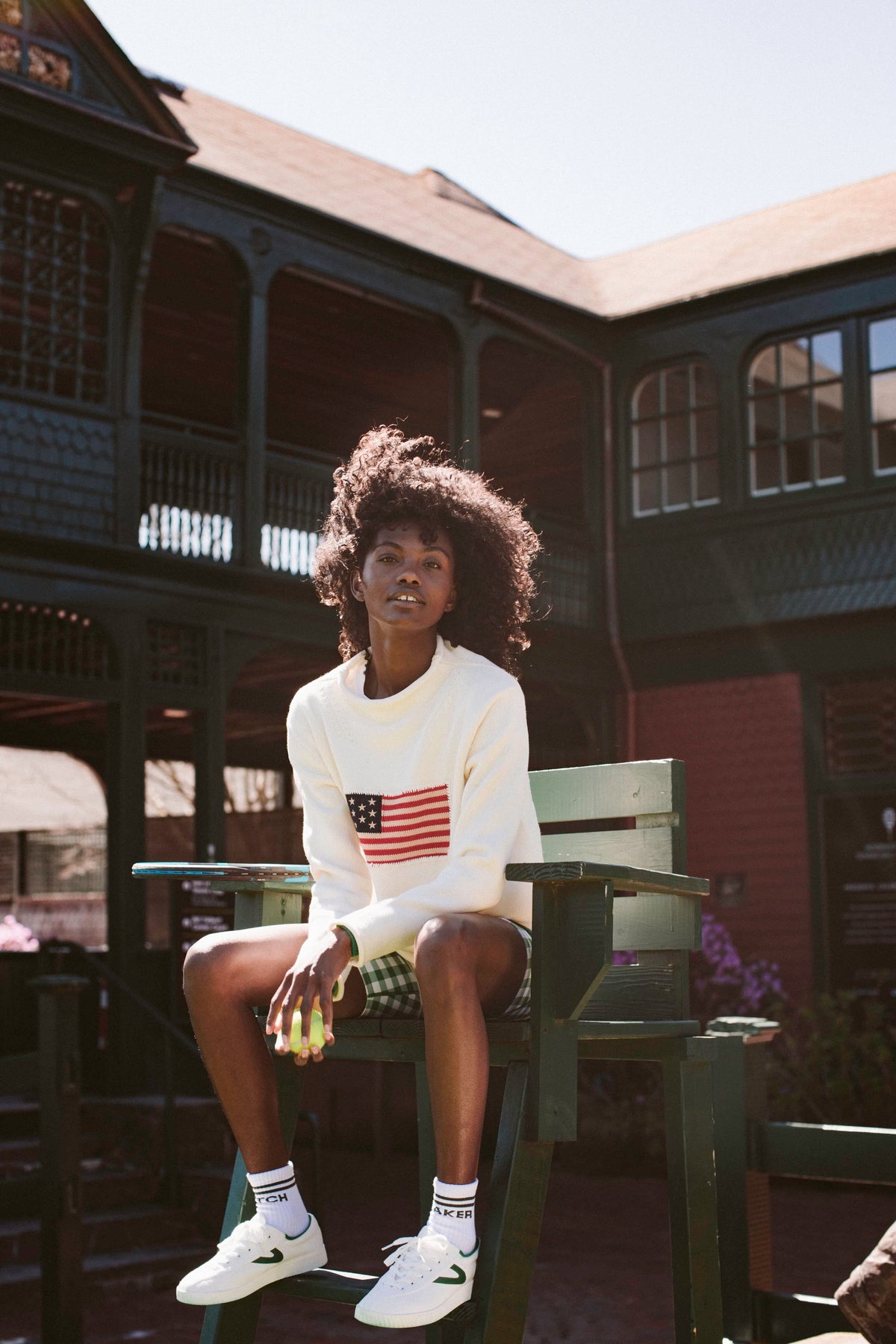 Woman sitting on a green chair in a white sweater with the American flag. 