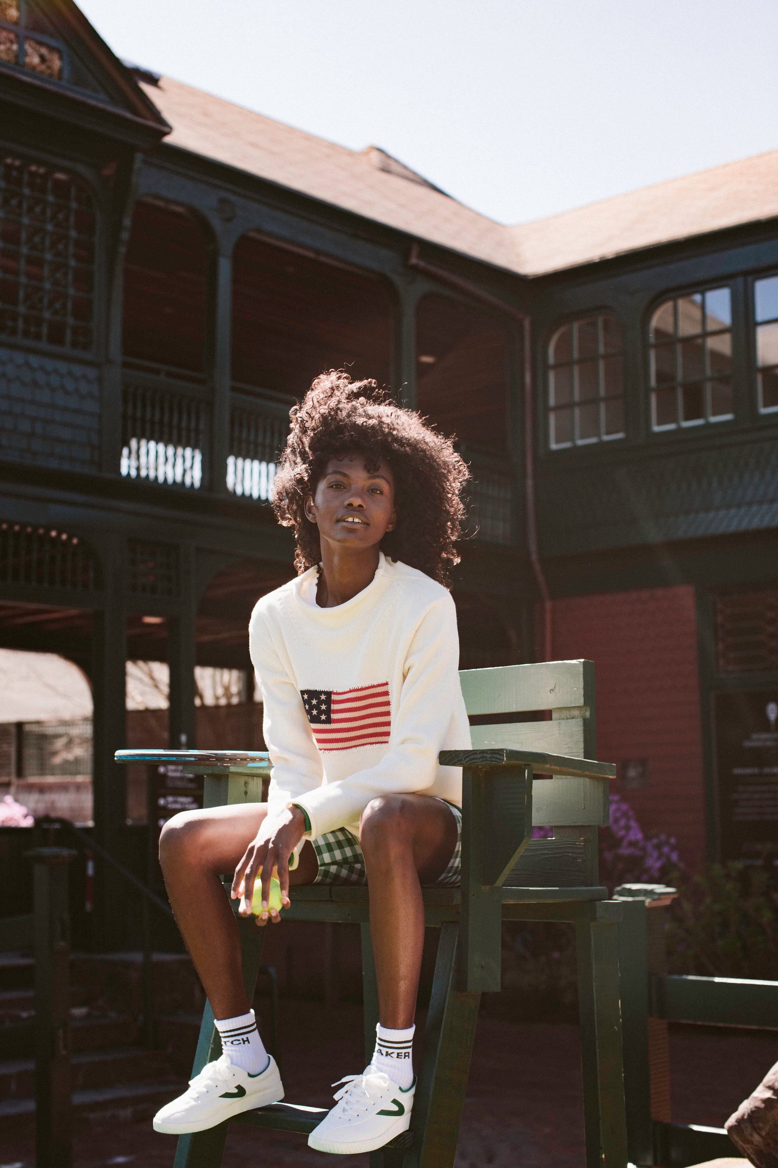 Woman sitting on a green chair in a white sweater with the American flag. 