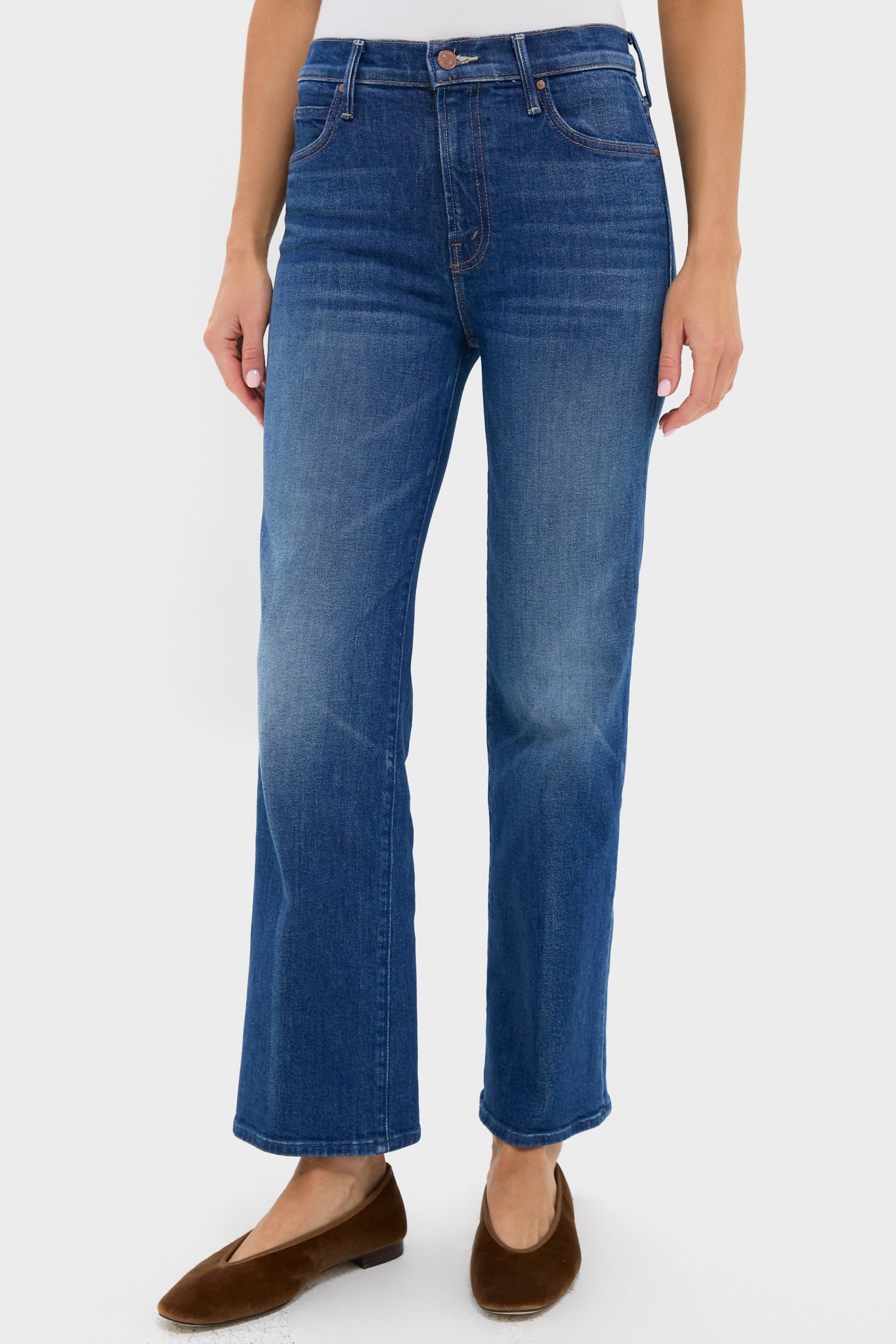 A person wears high-rise straight leg jeans by MOTHER and brown flats, standing in a simple white setting.