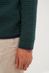 A close-up of a person's arm wearing a Peter Millar dark green quarter-zip in textured cotton-performance fabric and beige pants, with their hand visible.