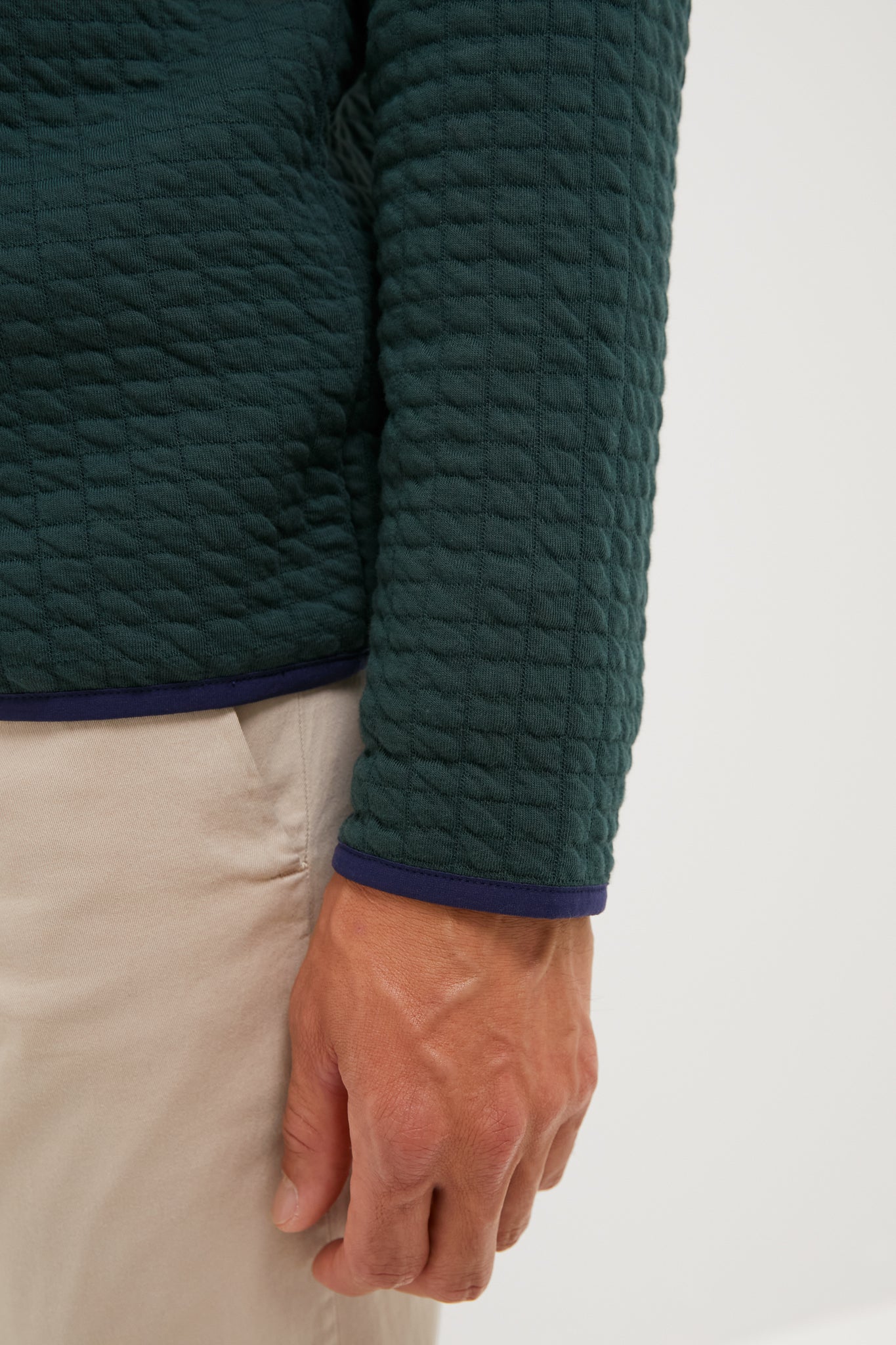 A close-up of a person's arm wearing a Peter Millar dark green quarter-zip in textured cotton-performance fabric and beige pants, with their hand visible.