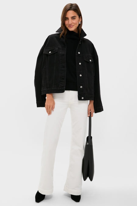 A woman stands against a plain background wearing a black denim jacket, black top, ASKK NY high-rise wide leg pants, black shoes, and holding a black tote bag from ASKK NY.