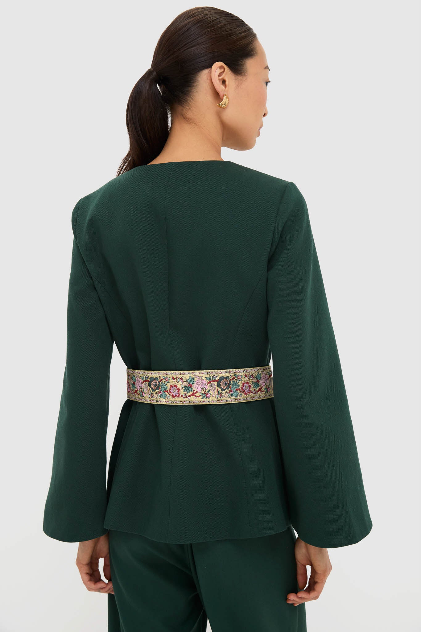 Back view of a model in a classic, high-end Garden Scrollwork Jacquard Belted Rhoda Tunic Top, showcasing effortless elegance with fun, flared sleeves and a sculptural earring.