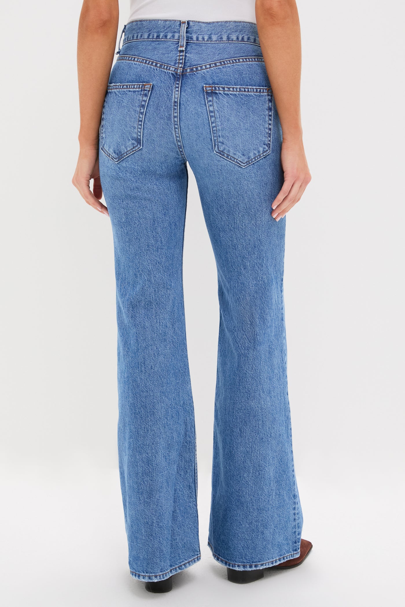 A person is shown from the back against a plain white background, wearing ASKK NY high-rise flare jeans in vintage-inspired blue denim and a grey top.
