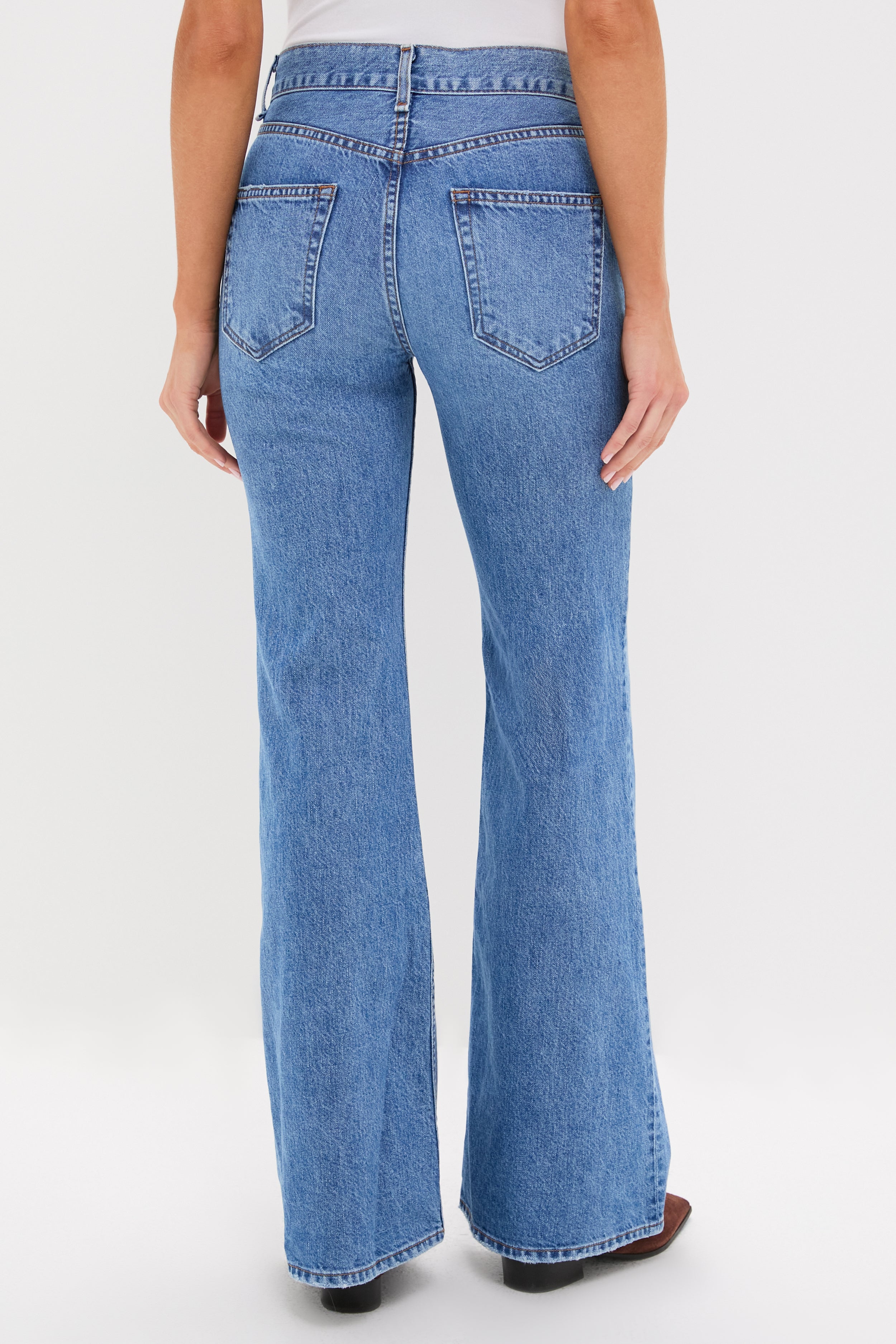 A person is shown from the back against a plain white background, wearing ASKK NY high-rise flare jeans in vintage-inspired blue denim and a grey top.
