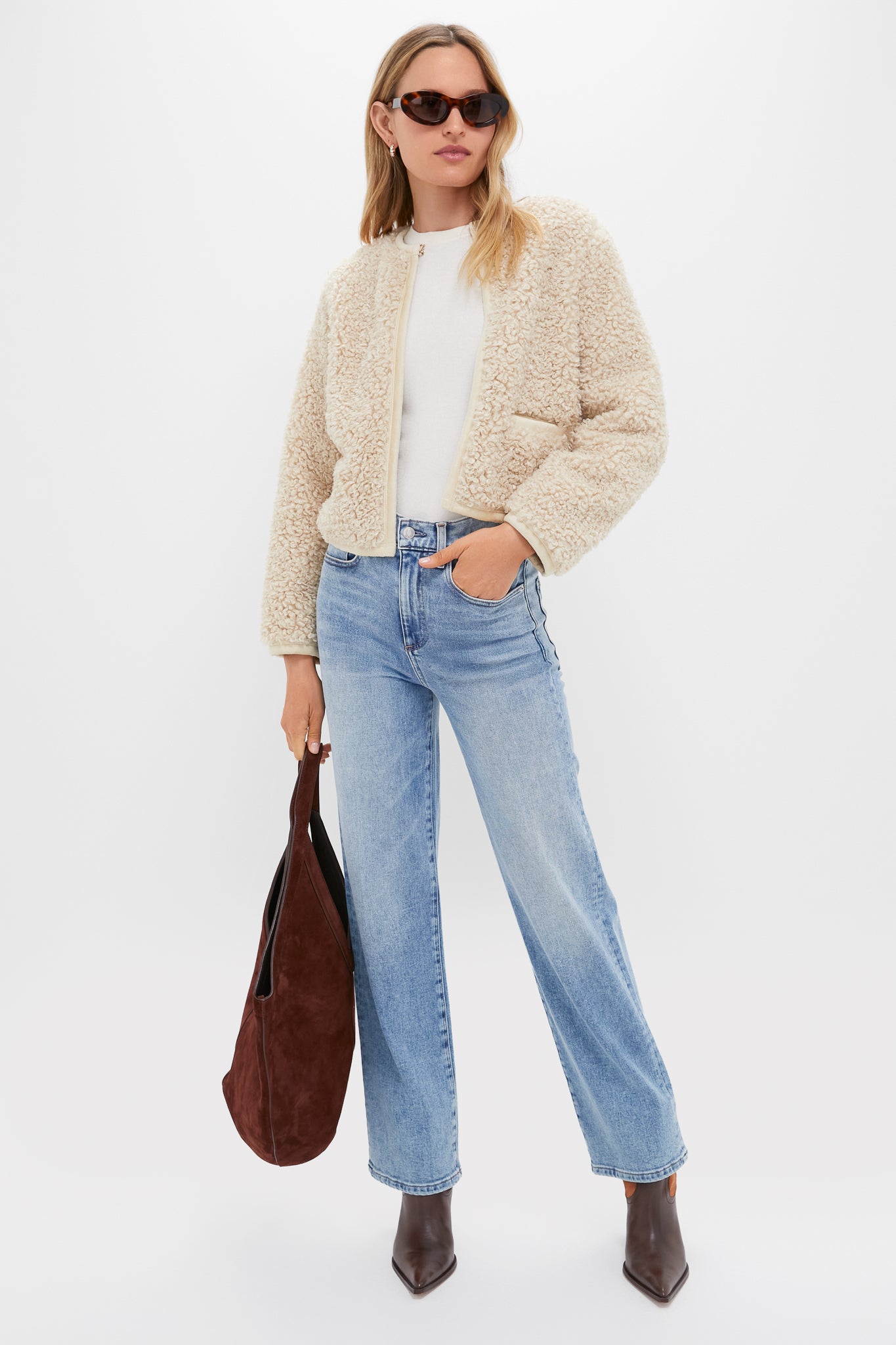 Woman effortlessly styled in Tortoise Roma Sunglasses with chic oval frames, exuding a classic, high-end vibe, paired with a sherpa jacket and slouchy suede tote.