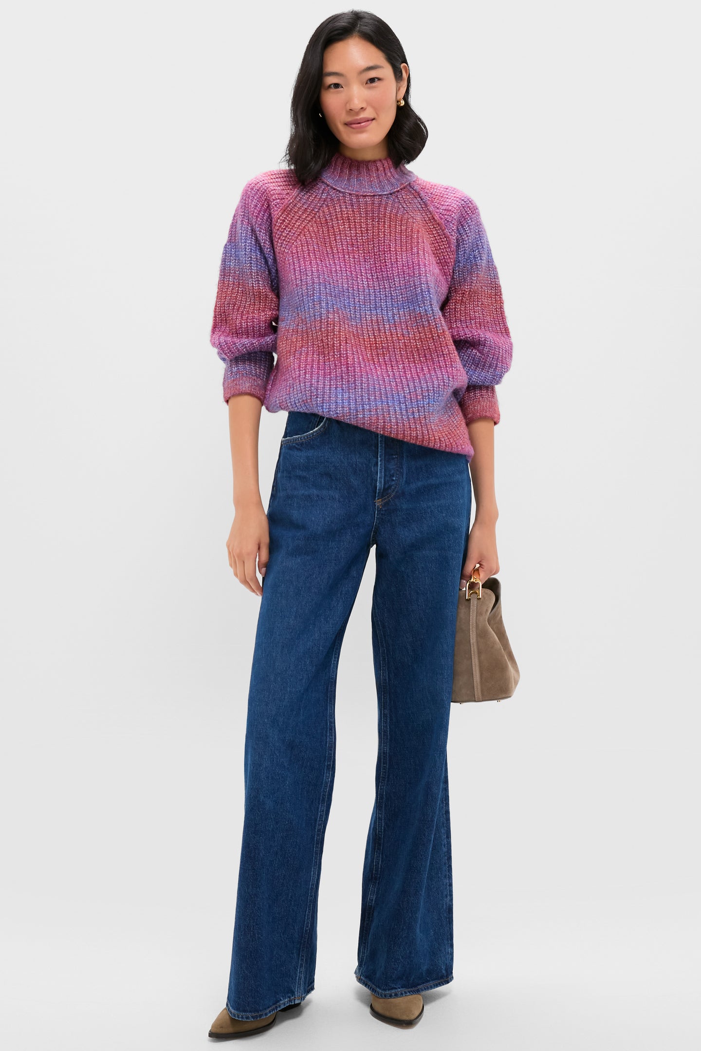 Woman in a casual outfit wears a pink and purple knit sweater, wide-leg blue jeans, brown shoes, and carries an Elleme small suede bag with a metal top handle.
