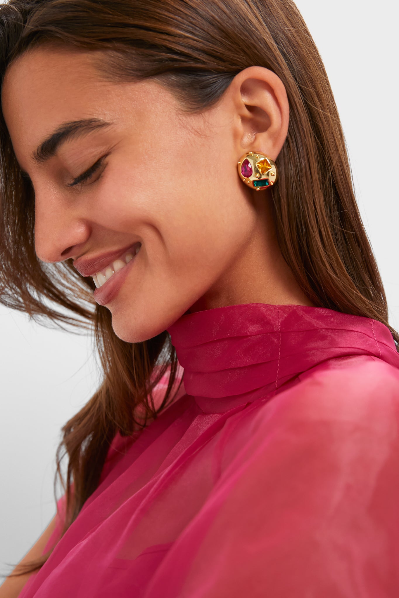 Woman wearing Mixed Crystal Lucy Studs, gold round earrings with multicolored gemstones, paired with a sheer fuchsia top, embodying a classic, effortless, and high-end style.