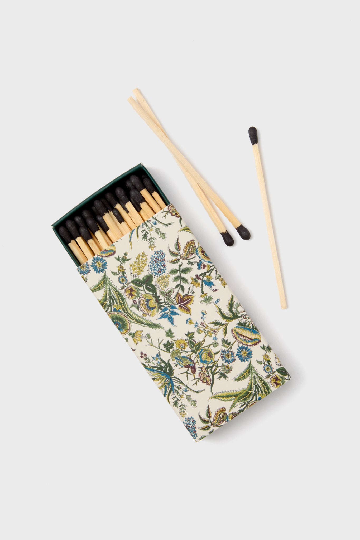 An open Tuckernuck Home matchbox with a sharp floral print displays several matches inside, while three more rest beside it—an ideal accessory for any candle lover.