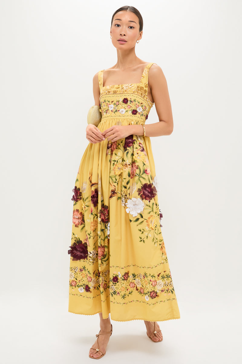 Woman wearing the Paramo Barbara Maxi Dress, a classic and effortless yellow gown with floral prints, holding a woven clutch, embodying a high-end, fun style.