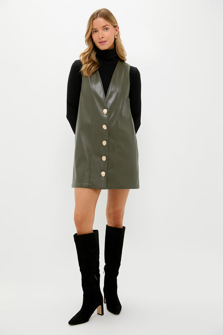 Model in a classic olive faux leather pinafore dress over a black turtleneck, styled with knee-high suede boots, embodying effortless, fun, high-end fashion.