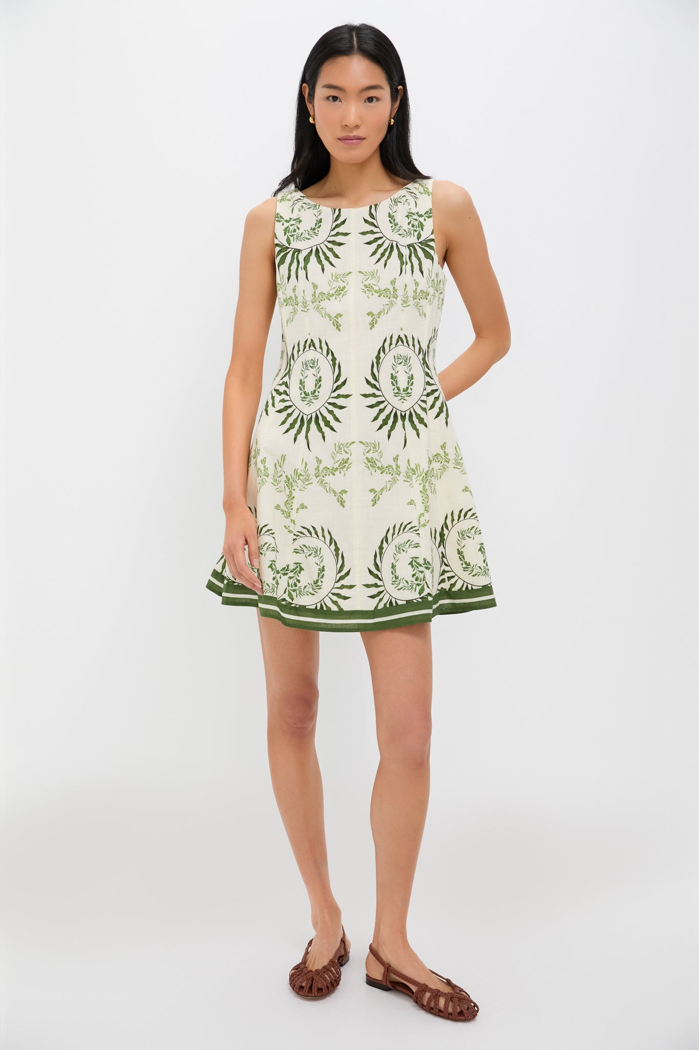 Young woman models the Ireland Green Layla Mini Dress, featuring classic botanical motifs and an effortless A-line silhouette, styled with fun brown sandals and gold hoops.