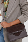 Person wearing a pin-striped blazer holds the classic Brown Leather Stevie Crossbody, featuring an effortless, high-end design with woven suede flap and smooth leather body.