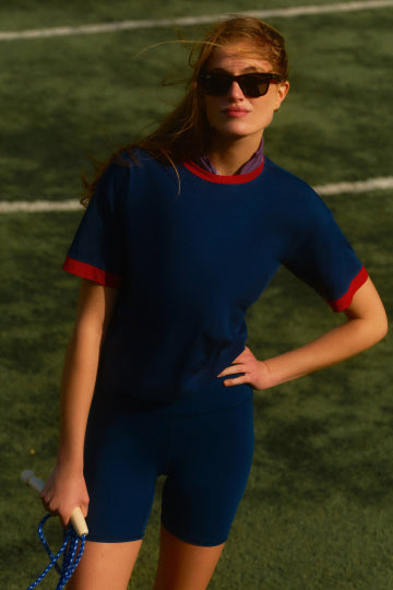 Woman standing on a field in a navy tee with red trim and navy bike shorts. 