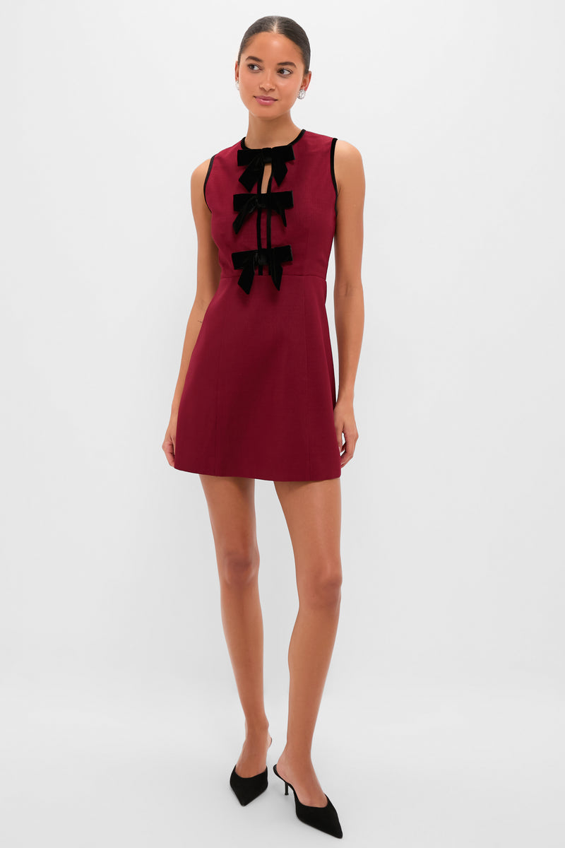 Woman modeling the Cranberry Velvet Bow Jaclyn Mini Dress, featuring a classic fitted bodice, three black velvet bows, and a slightly flared skirt, styled with effortless, fun elegance.