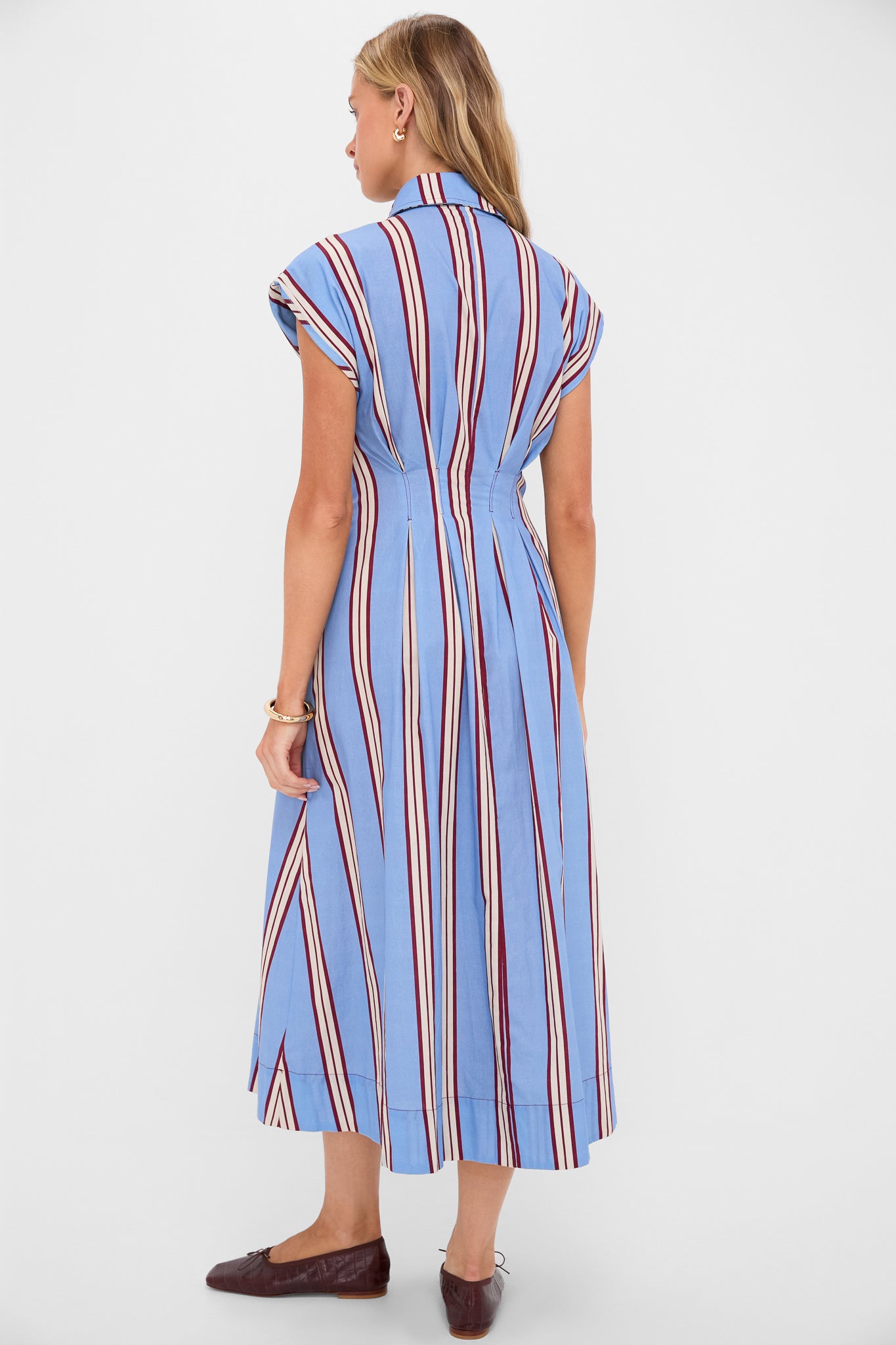 Young woman in a classic, effortless Striped Mirante Shirt Dress, featuring vertical stripes and pleats, paired with ballet-style loafers and gold accessories, exuding high-end, fun style.
