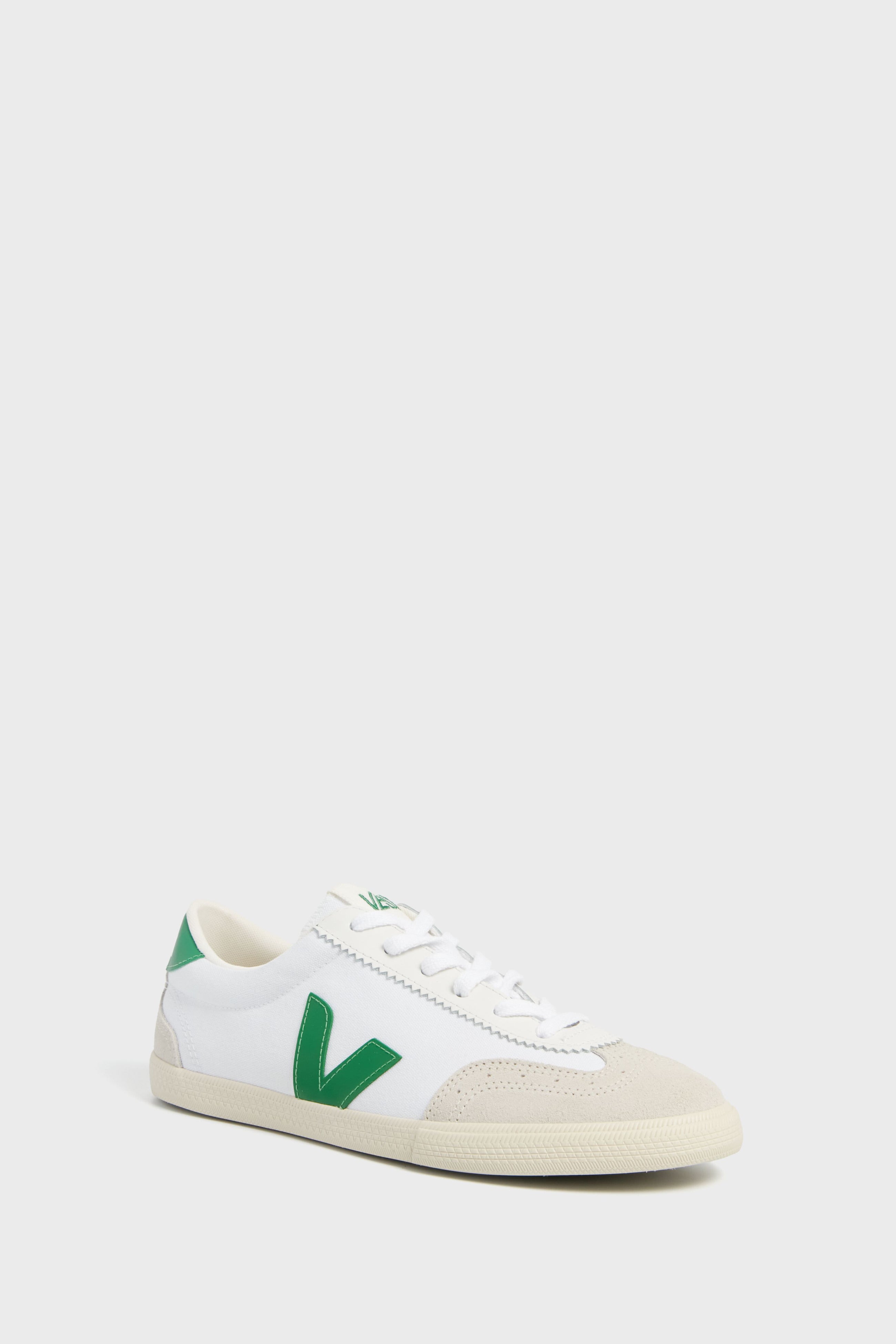 The VEJA sneaker features a white design with green accents, including a green V logo, white laces, and a beige toe cap. Made from sustainable materials.