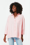 A woman wears a loose-fitting, light pink Pomander Place button-down shirt with a chest pocket and light blue jeans.