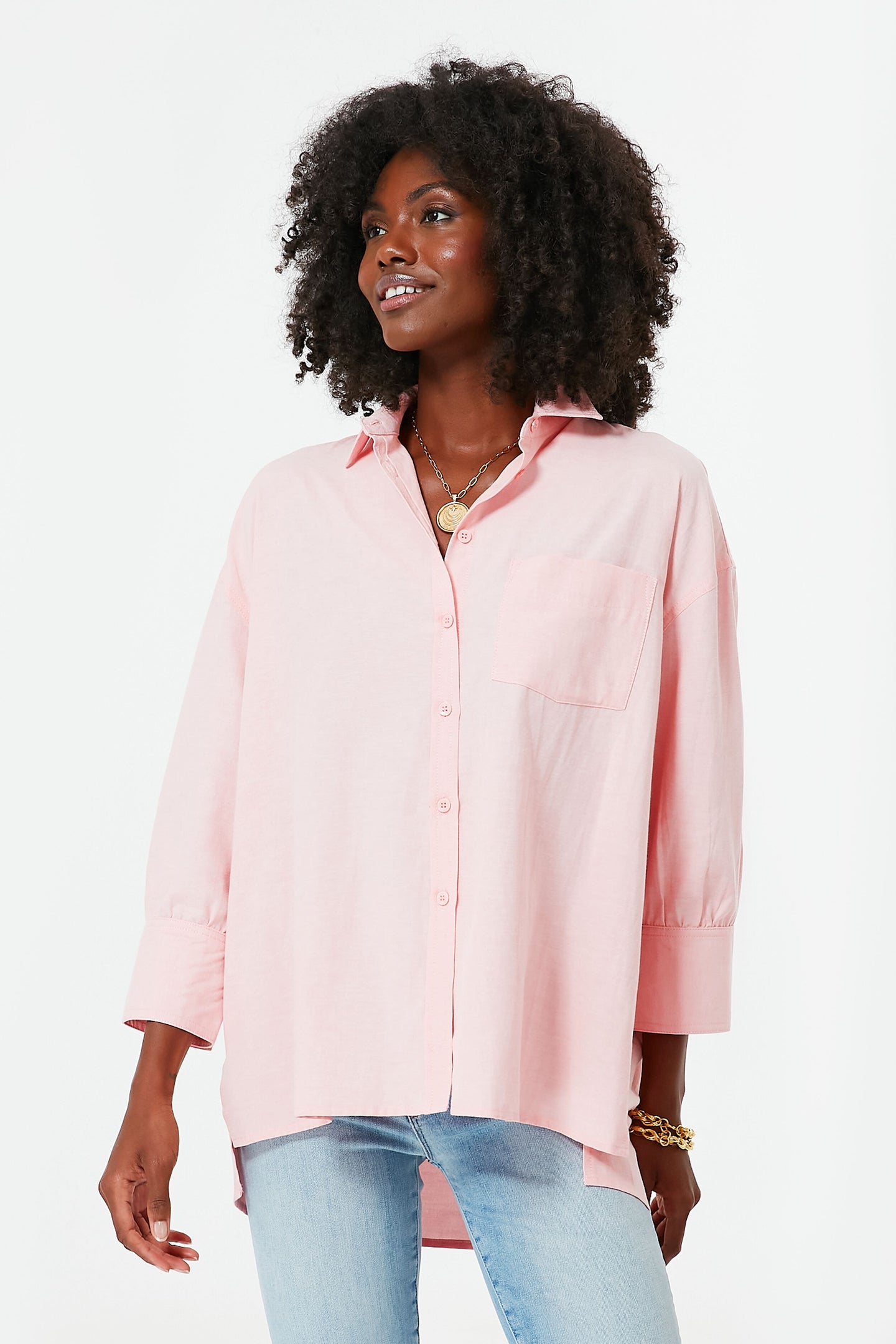 A woman wears a loose-fitting, light pink Pomander Place button-down shirt with a chest pocket and light blue jeans.