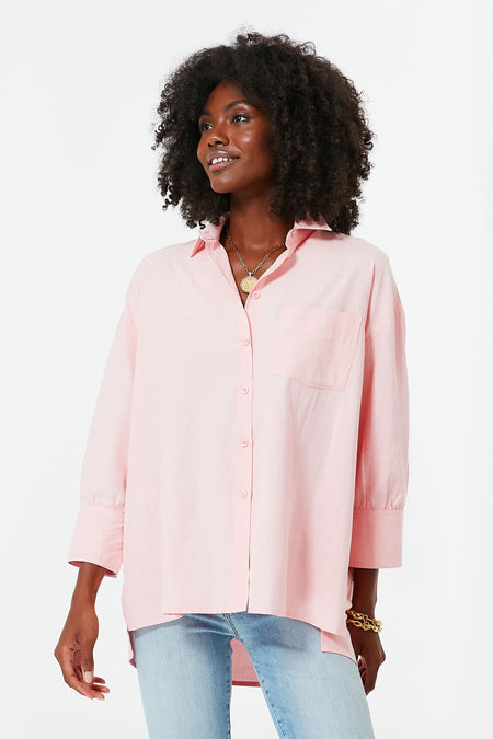 A woman wears a loose-fitting, light pink Pomander Place button-down shirt with a chest pocket and light blue jeans.