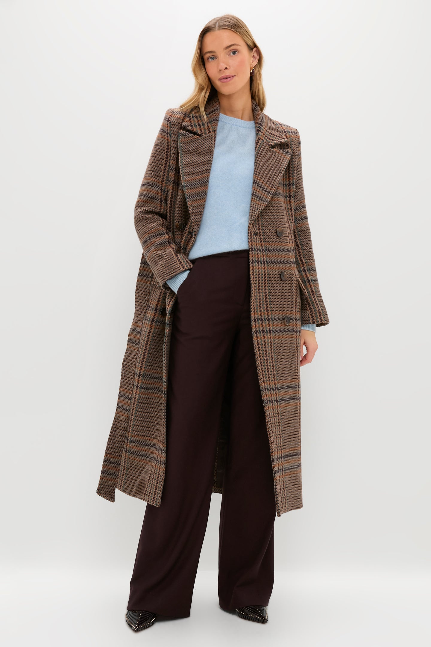 A woman models a L'AGENCE brown plaid coat layered over a light blue sweater and dark wide-leg pants, set against a plain light background.