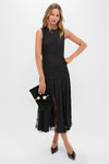 Model wearing the Black Mixed-Media Coco Maxi Dress, featuring a classic tunic-style bodice, lace-paneled pleats, and an effortless, high-end look with a suede clutch.