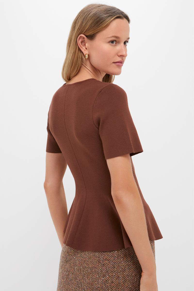 Model wearing the Chocolate Brown Knit Phoebe Peplum Top, featuring a round neck and peplum hem, paired with a herringbone skirt and gold hoop earring. Classic and effortless.