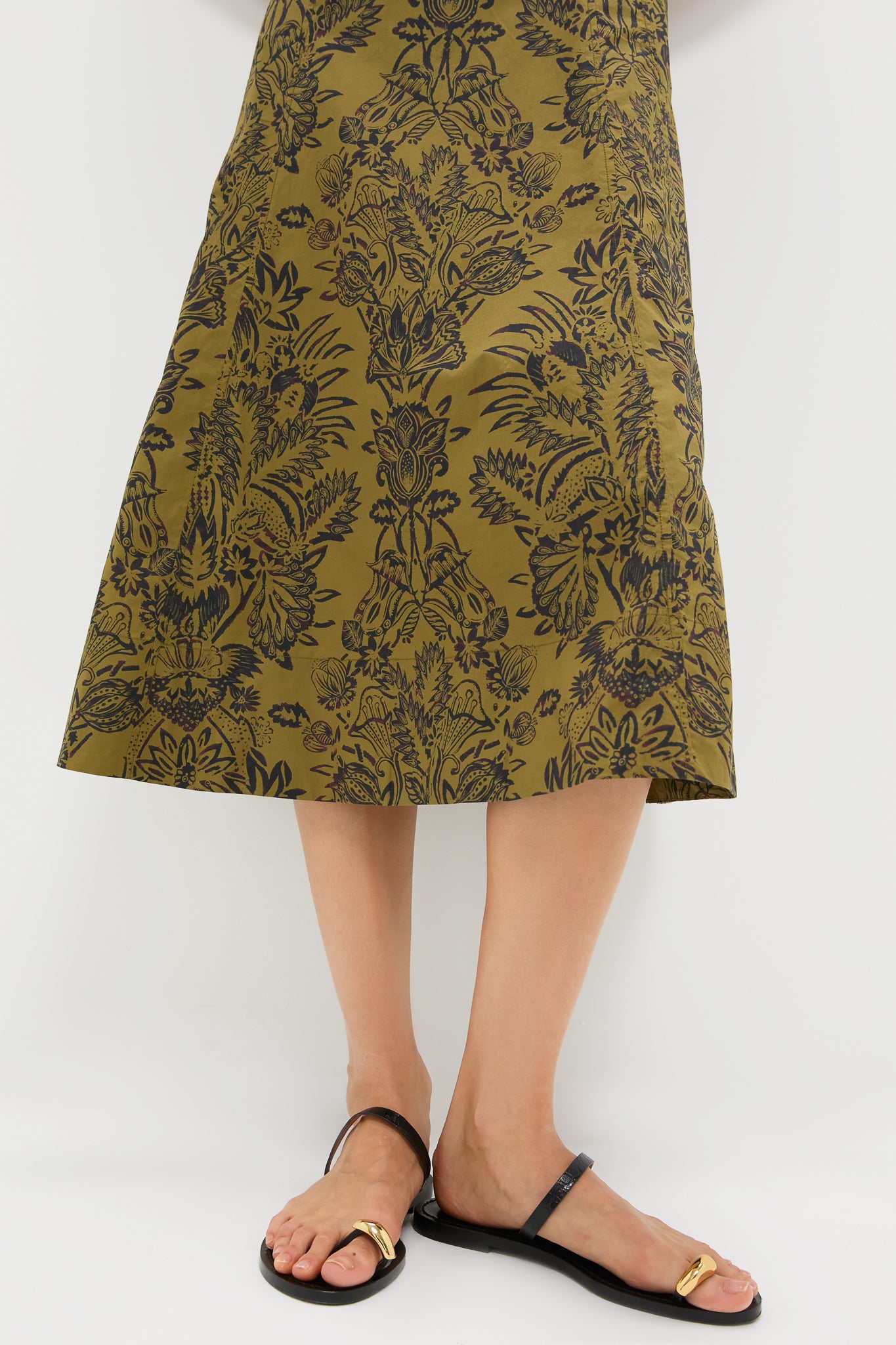 Olive Flora Natali Dress: A classic, high-end calf-length skirt with an effortless olive-green and black floral pattern, paired with minimalist black sandals featuring a fun gold buckle.