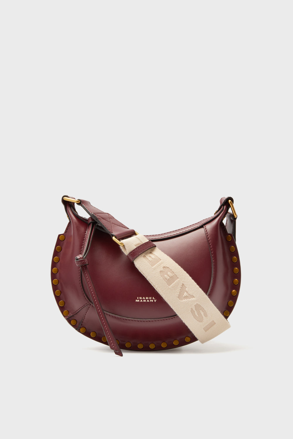 A burgundy leather Isabel Marant Mini Moon Crossbody with gold stud accents, a wide beige ISABEL strap, and a front zipper pocket.