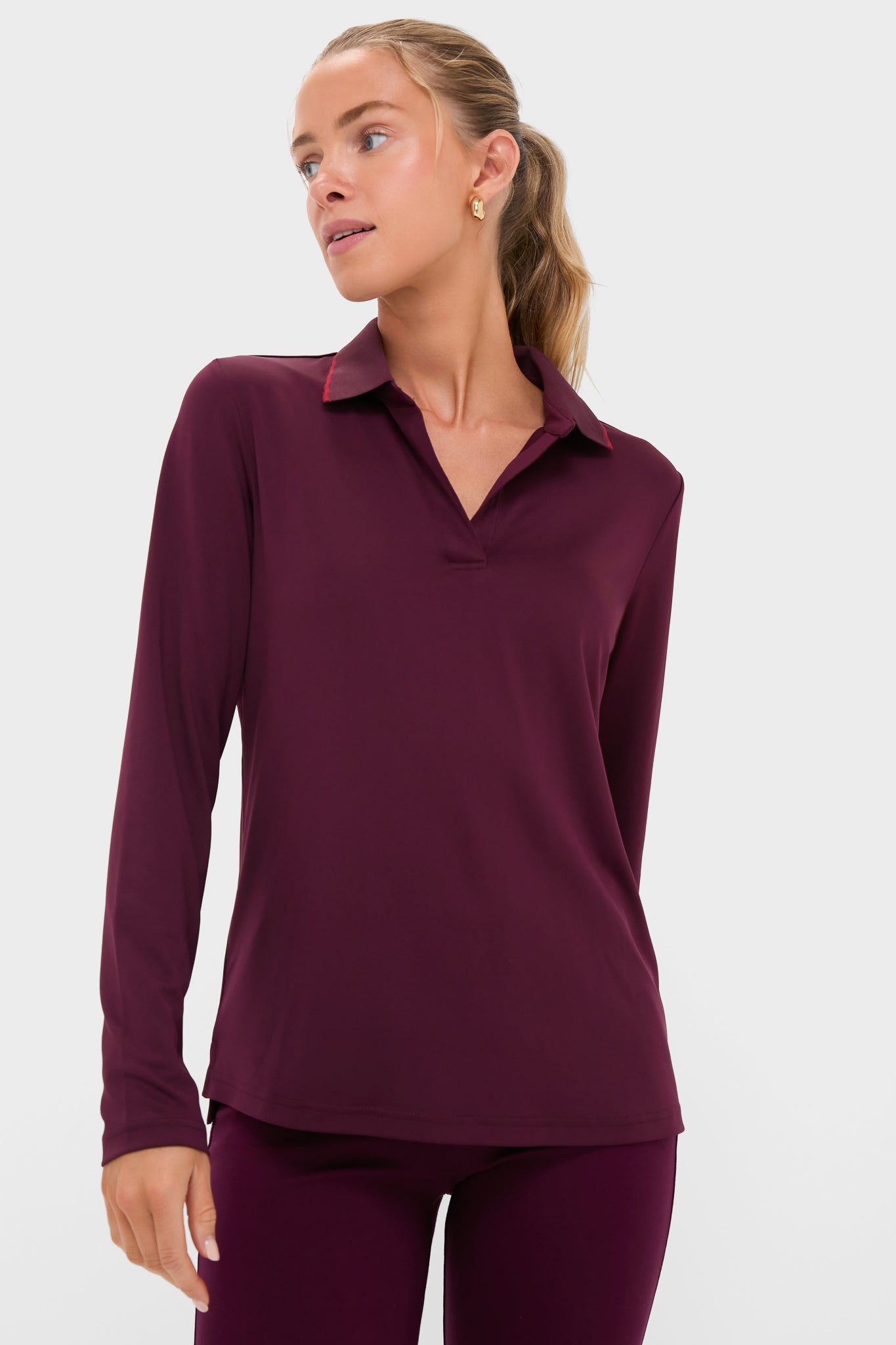 A woman wearing a Tnuck Sport long-sleeve burgundy slim fit polo and matching SPF-protective pants looks to her left.
