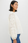 Woman models the classic Ivory Patchwork Embroidered Cressida Blouse, featuring effortless puff sleeves and intricate embroidery, paired with jeans for a fun, high-end look.
