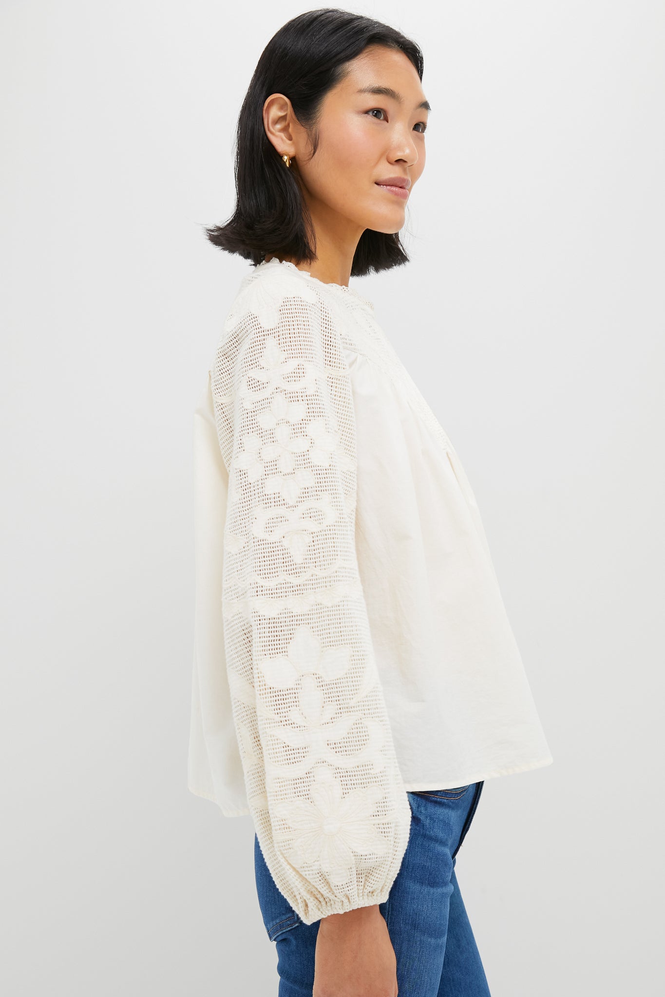 Woman models the classic Ivory Patchwork Embroidered Cressida Blouse, featuring effortless puff sleeves and intricate embroidery, paired with jeans for a fun, high-end look.