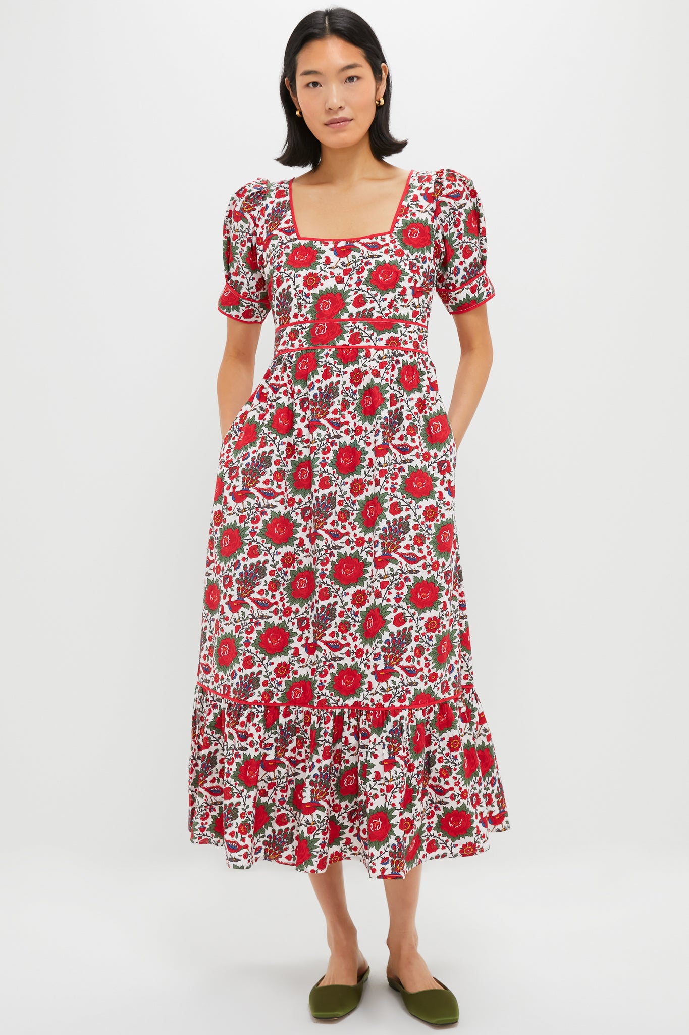 A woman wears a Pink City Prints red floral cotton poplin dress with short puff sleeves and a square neckline, paired with green flats.
